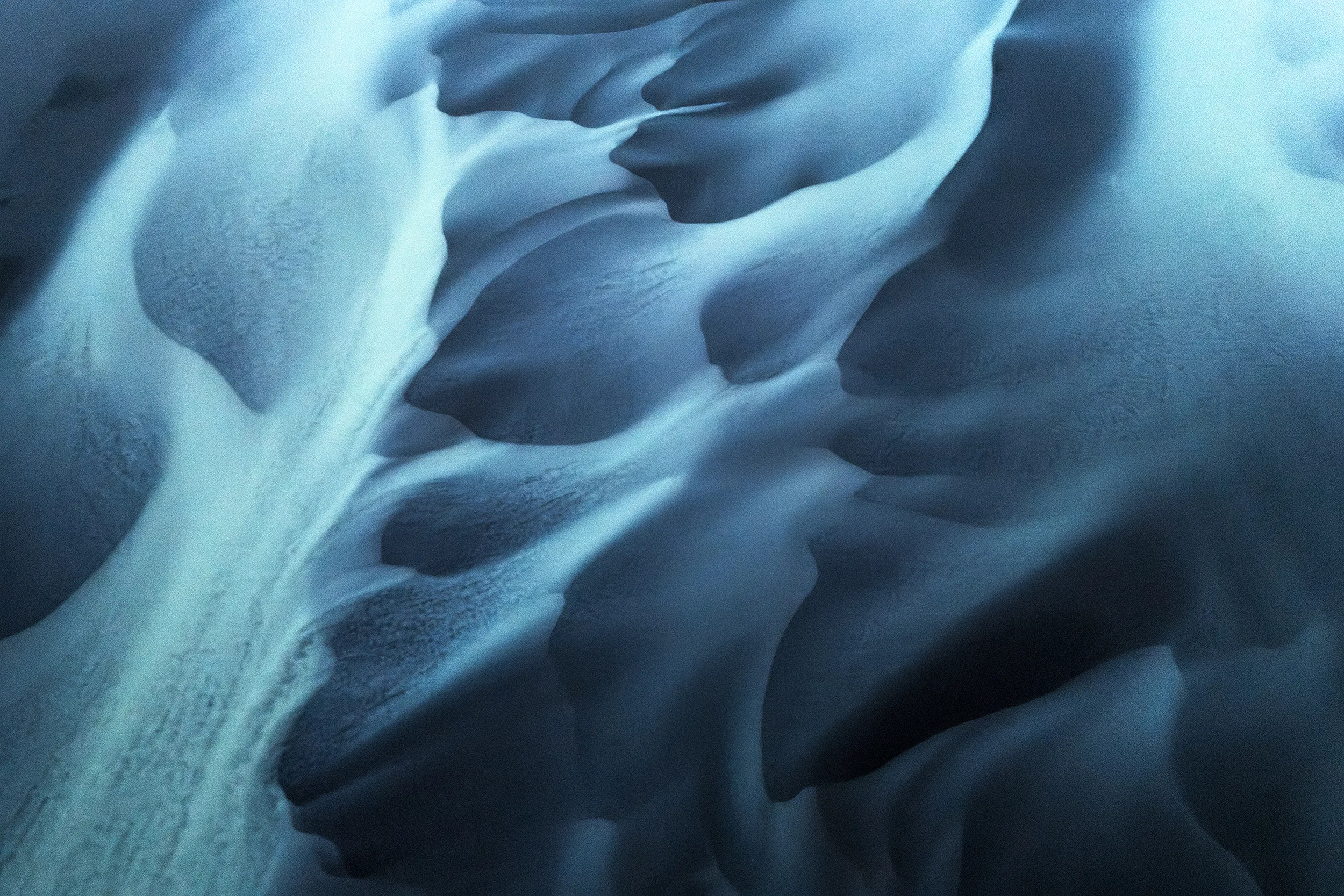 Close-up of snow and ice formations with smooth, curved surfaces in shades of blue and white.