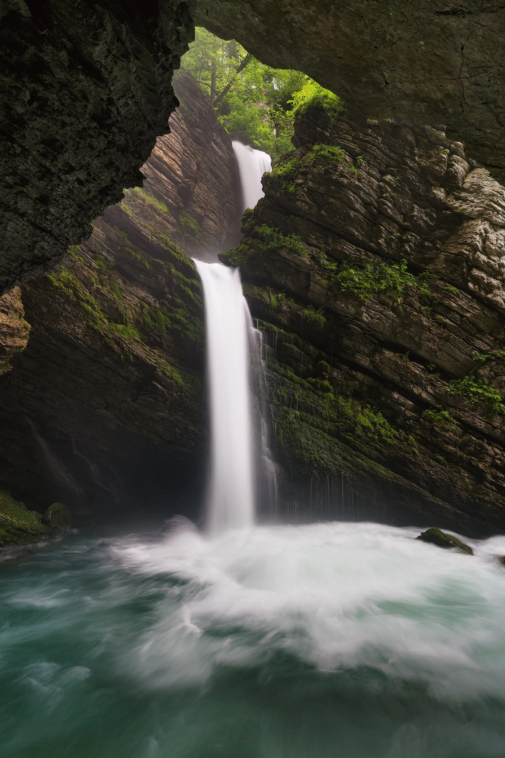 A waterfall into a pool, framed by the mouth of a rock cave.