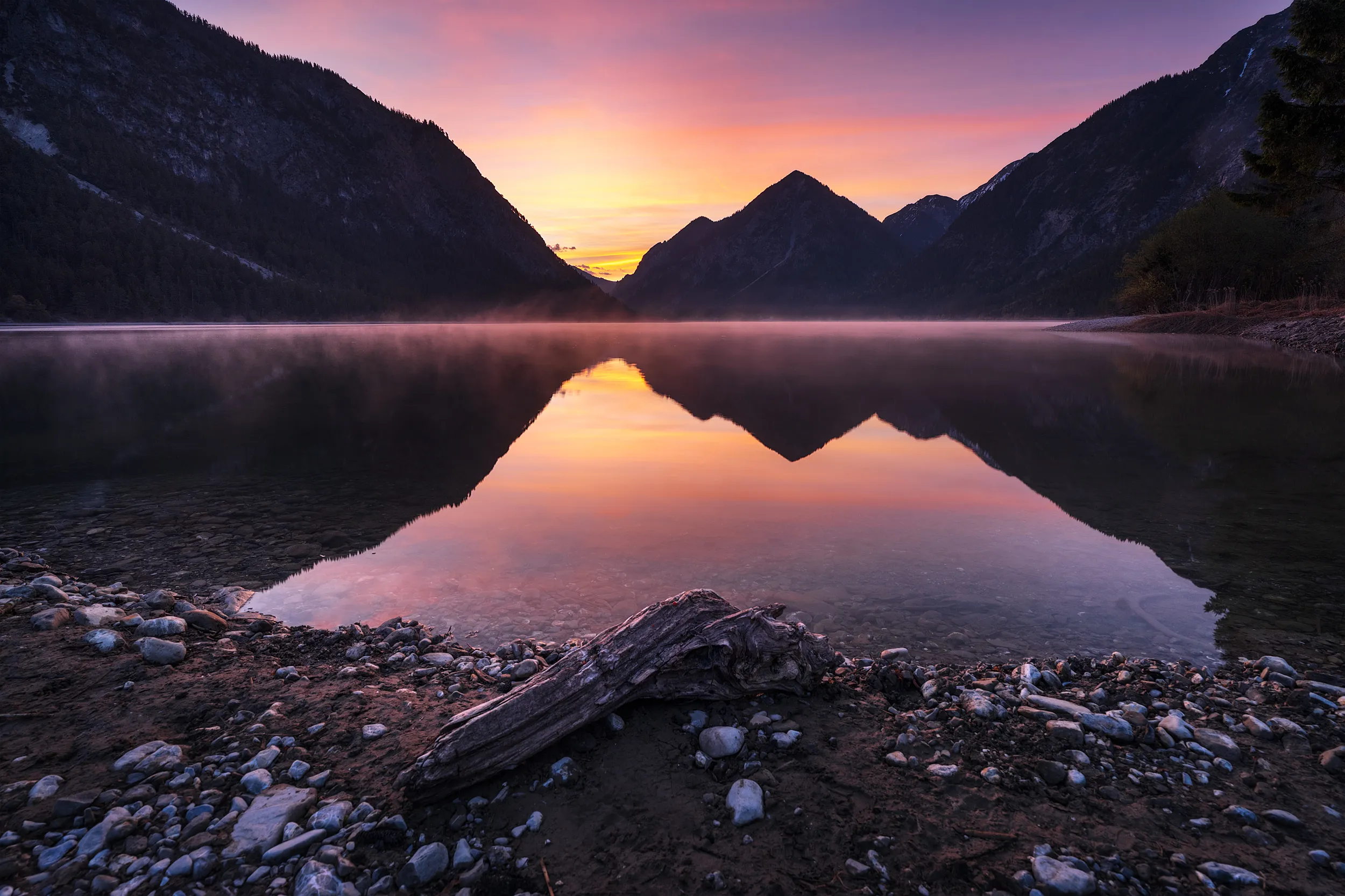 Calm lake at sunset reflecting the colorful sky and the surrounding mountains.