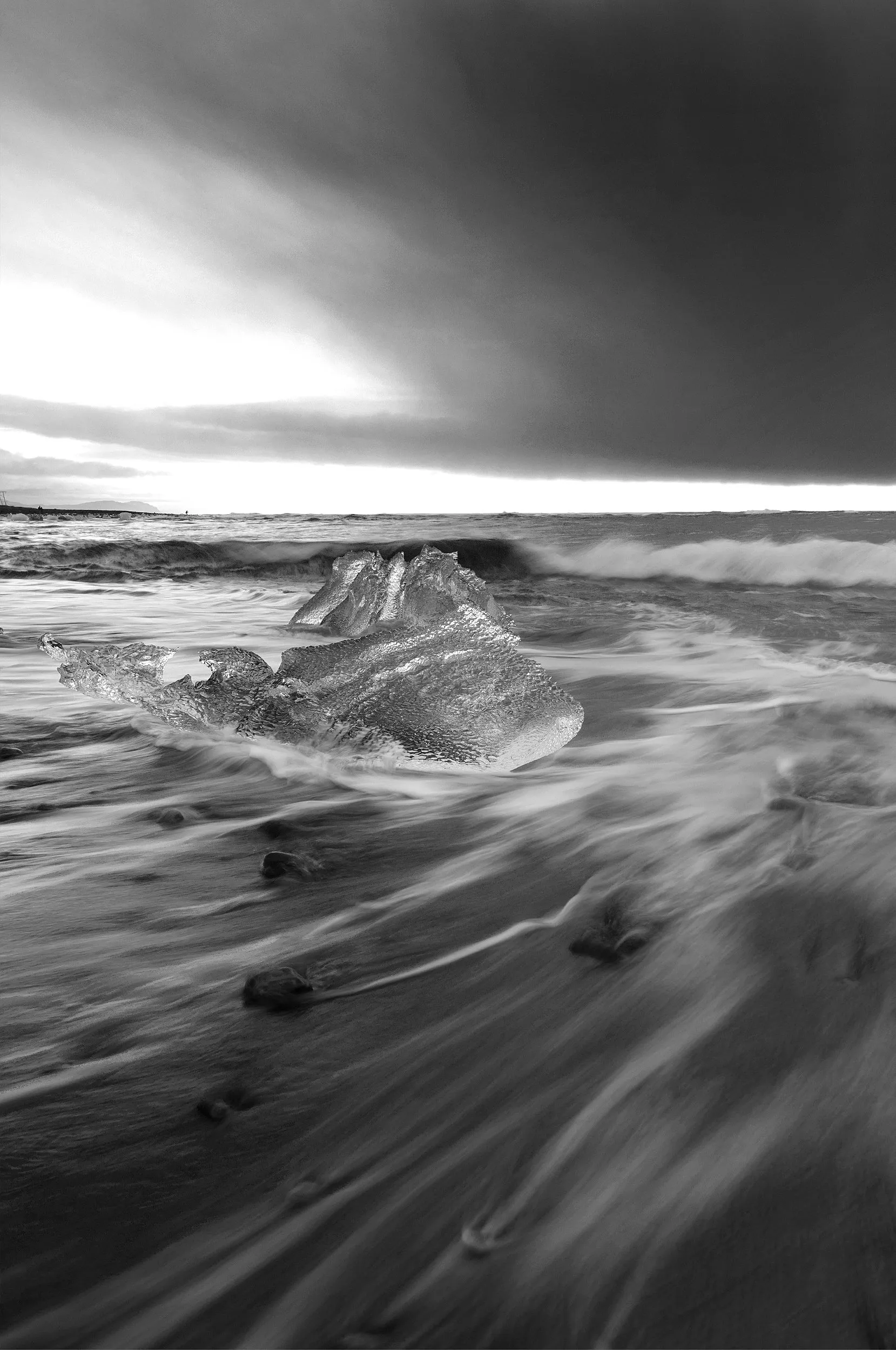 Surf against a rocky shore under dark cloud, in monochrome.