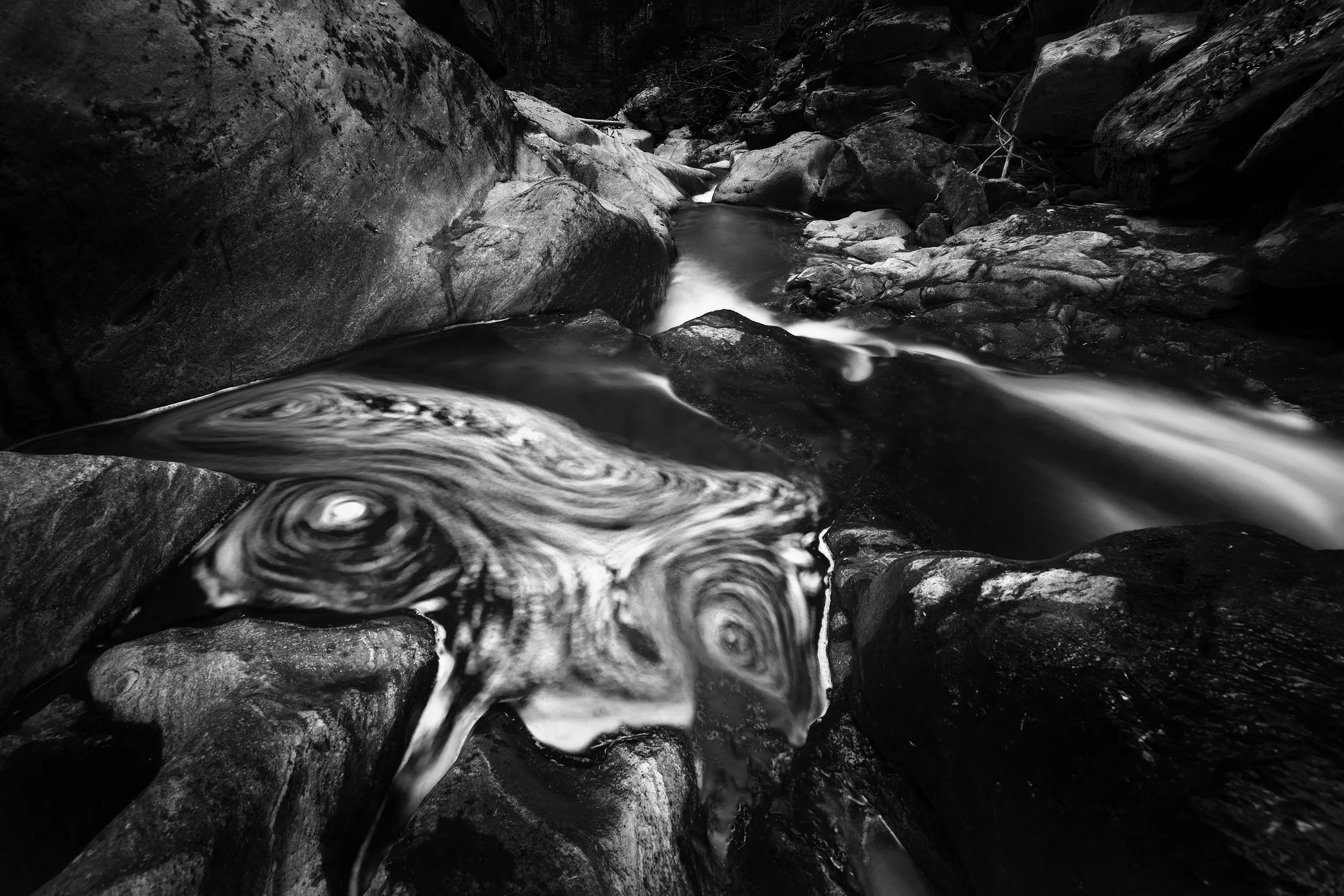 A mountain stream in swirling long-exposure patterns, in monochrome.