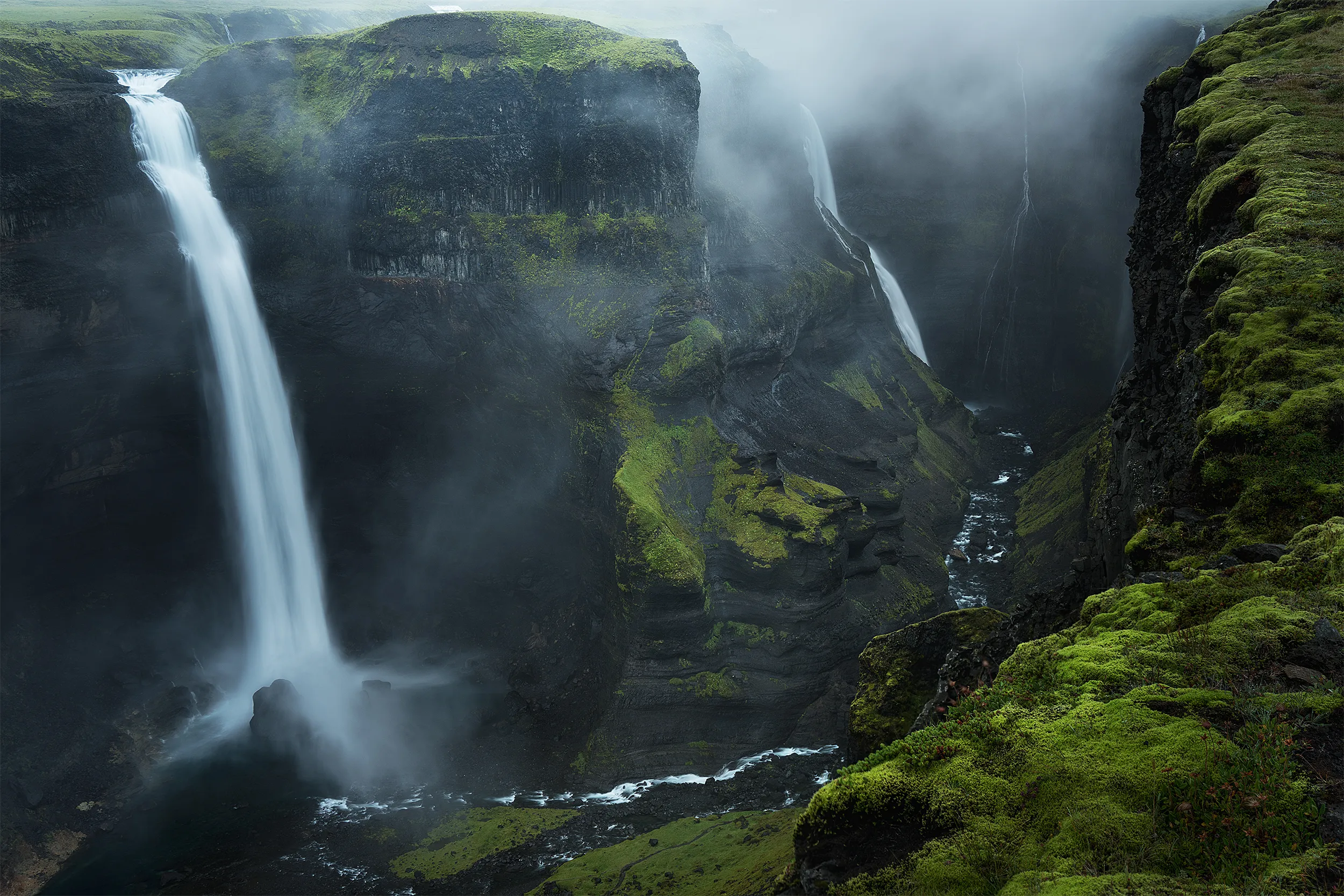 Waterfalls flowing down moss-covered cliffs, with mist rising from the water.