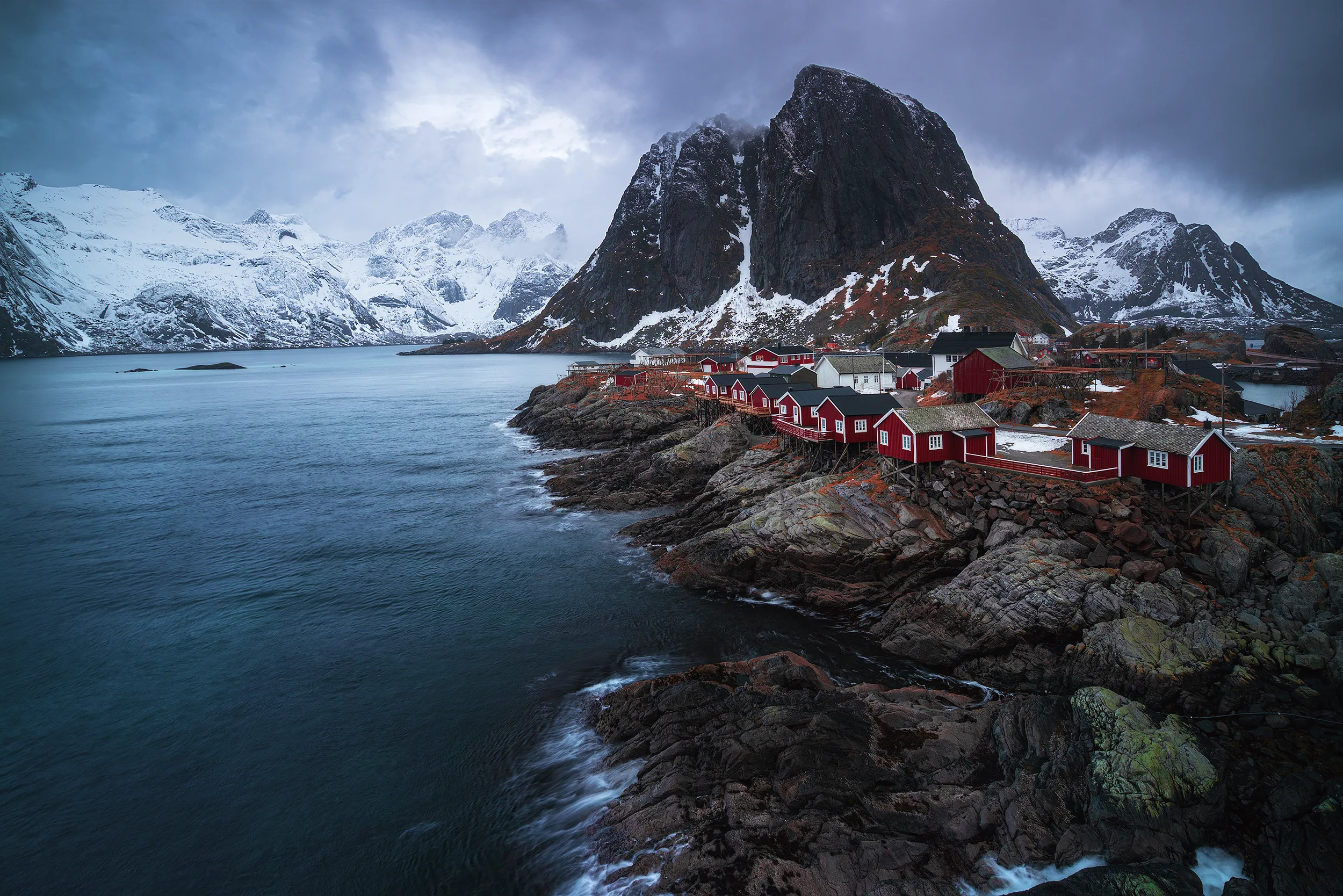 A fishing village of red houses beneath a snow-capped mountain.