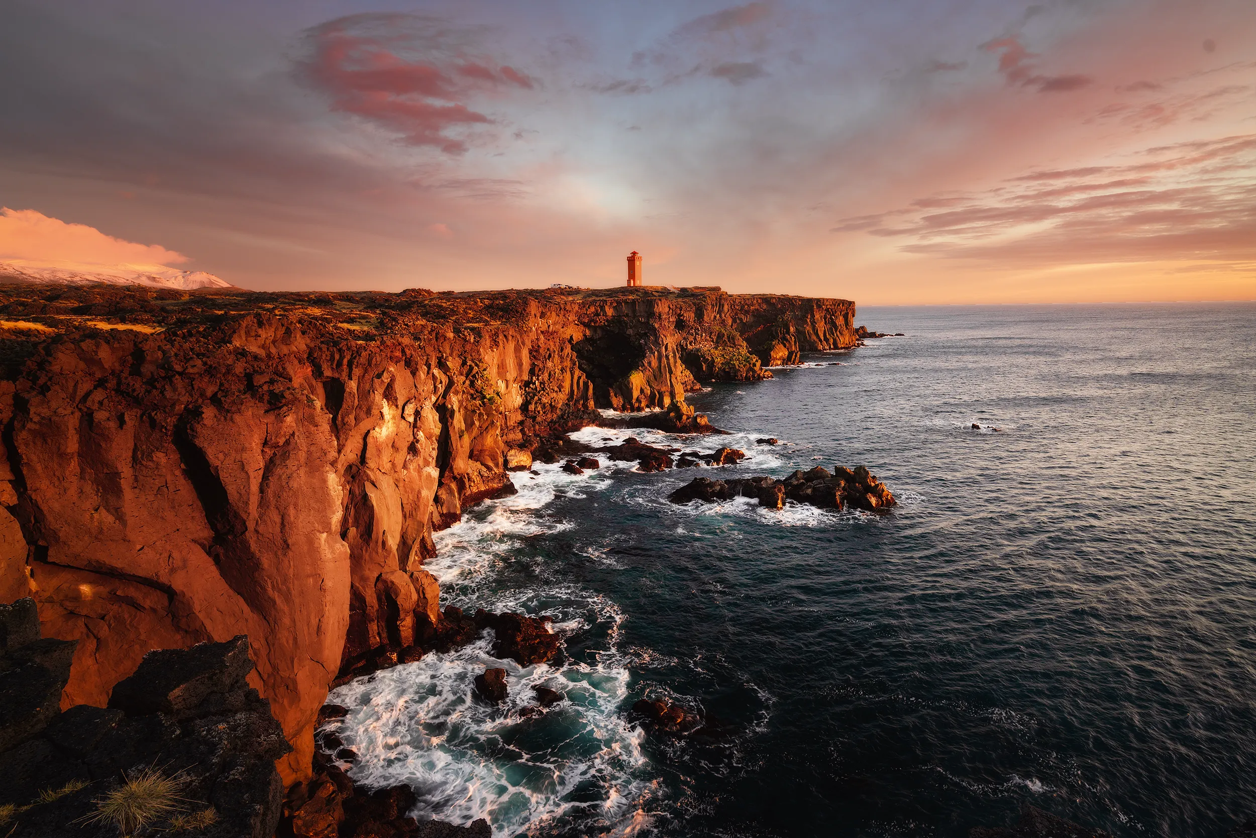 A lighthouse on a rugged cliff, waves breaking below in the evening light.