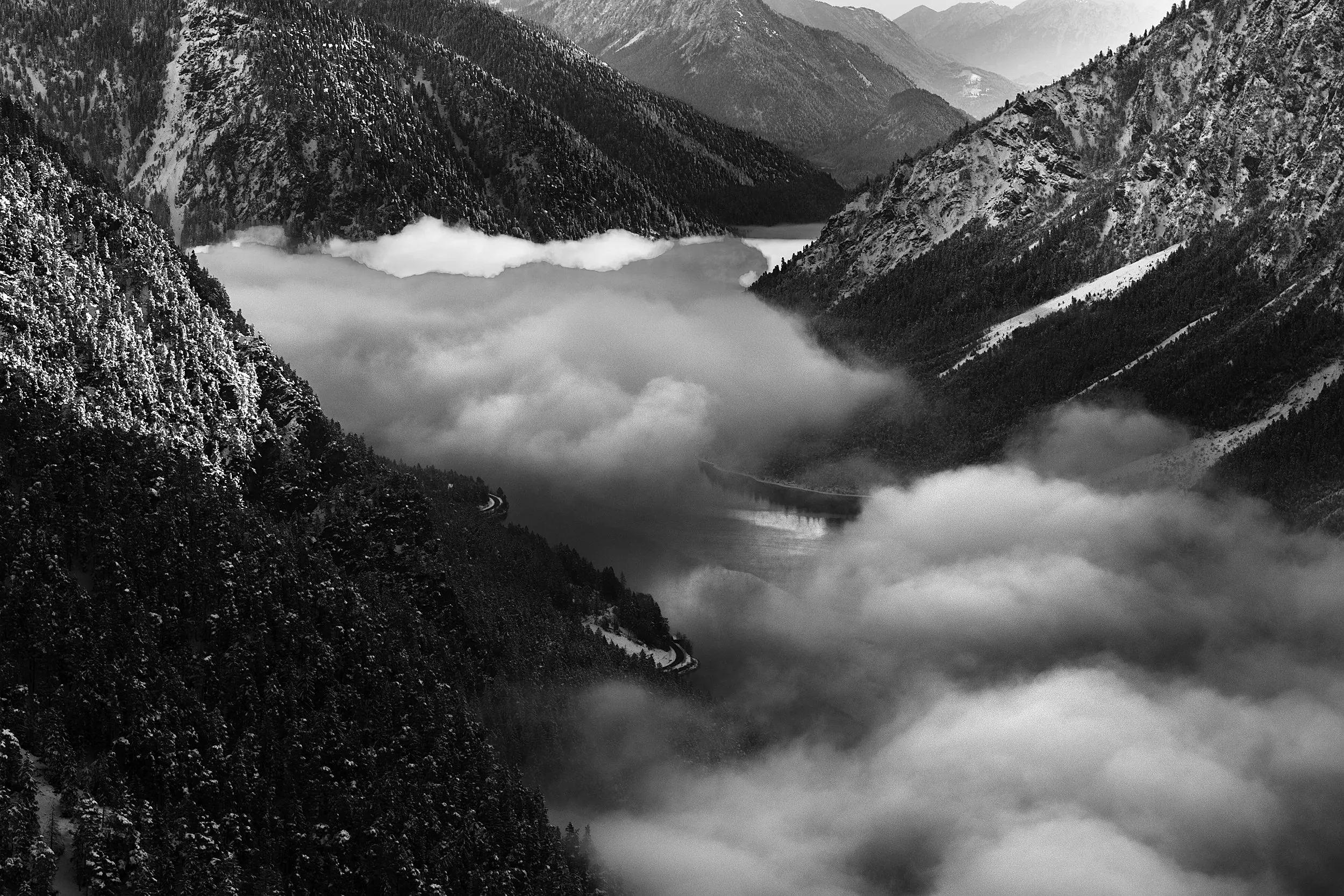 A steep, snow-capped mountain landscape in mist, in monochrome.