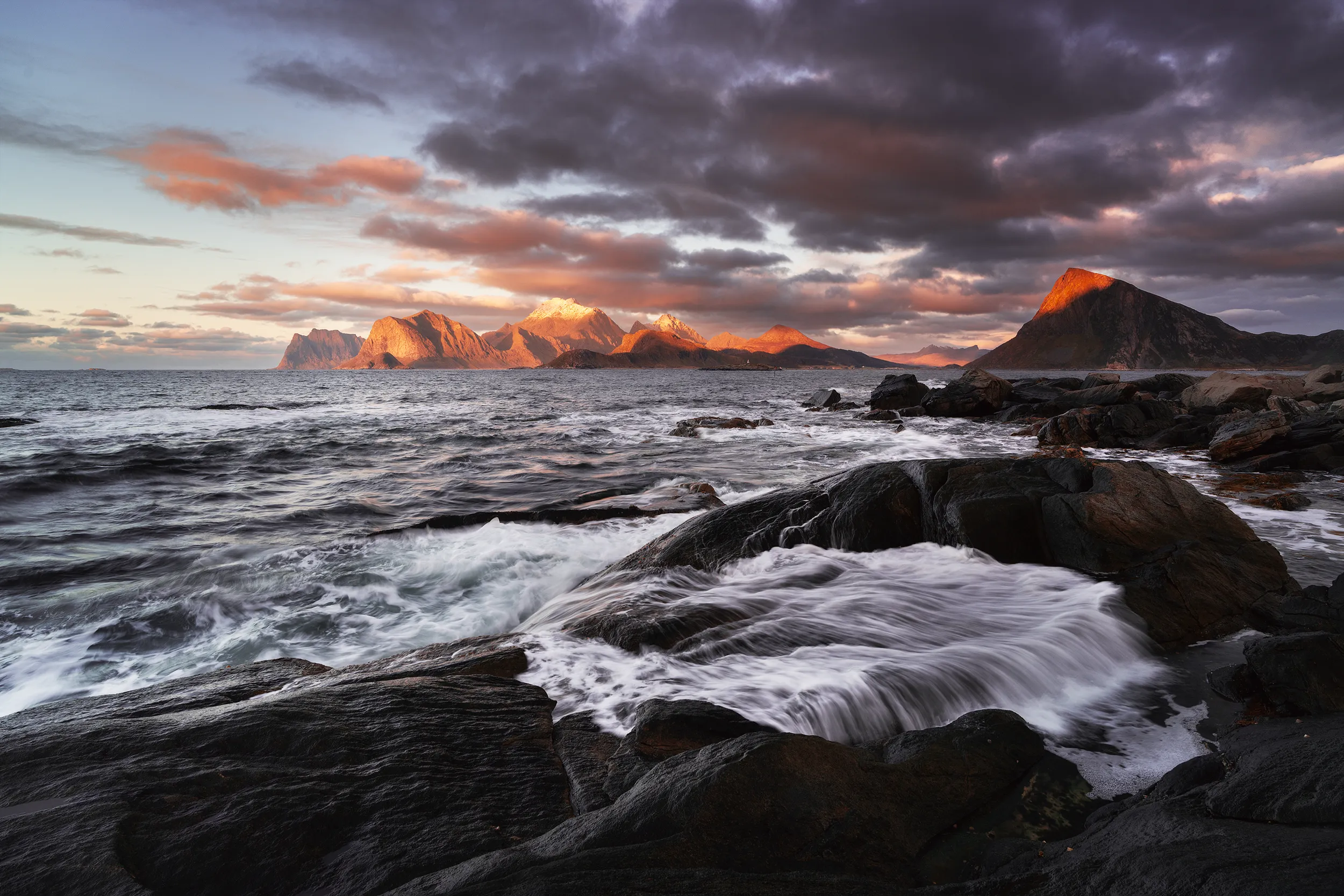 A rocky coastline beneath a dramatic sky at sunset.
