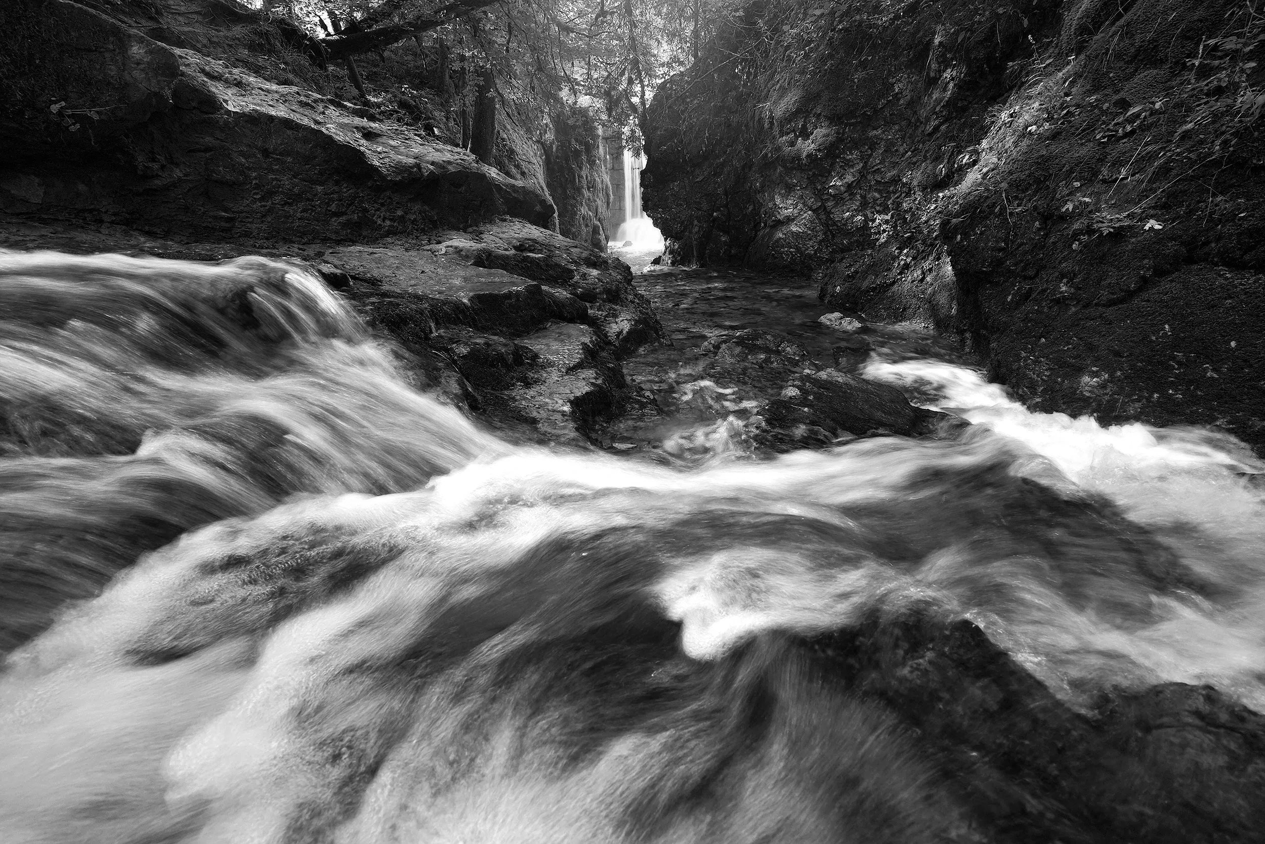 A fast mountain stream before a waterfall, in monochrome.
