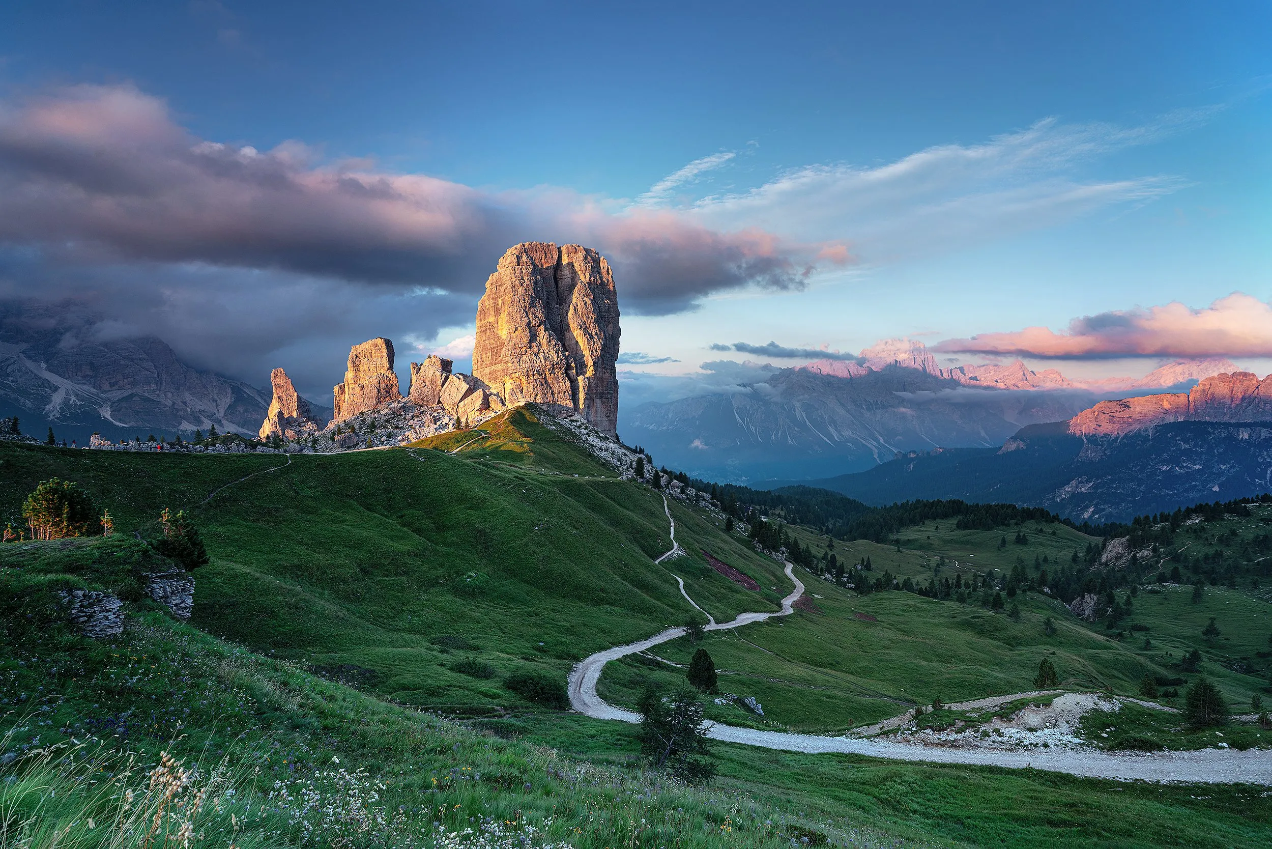 A dirt road winds through green hills toward rocky peaks.