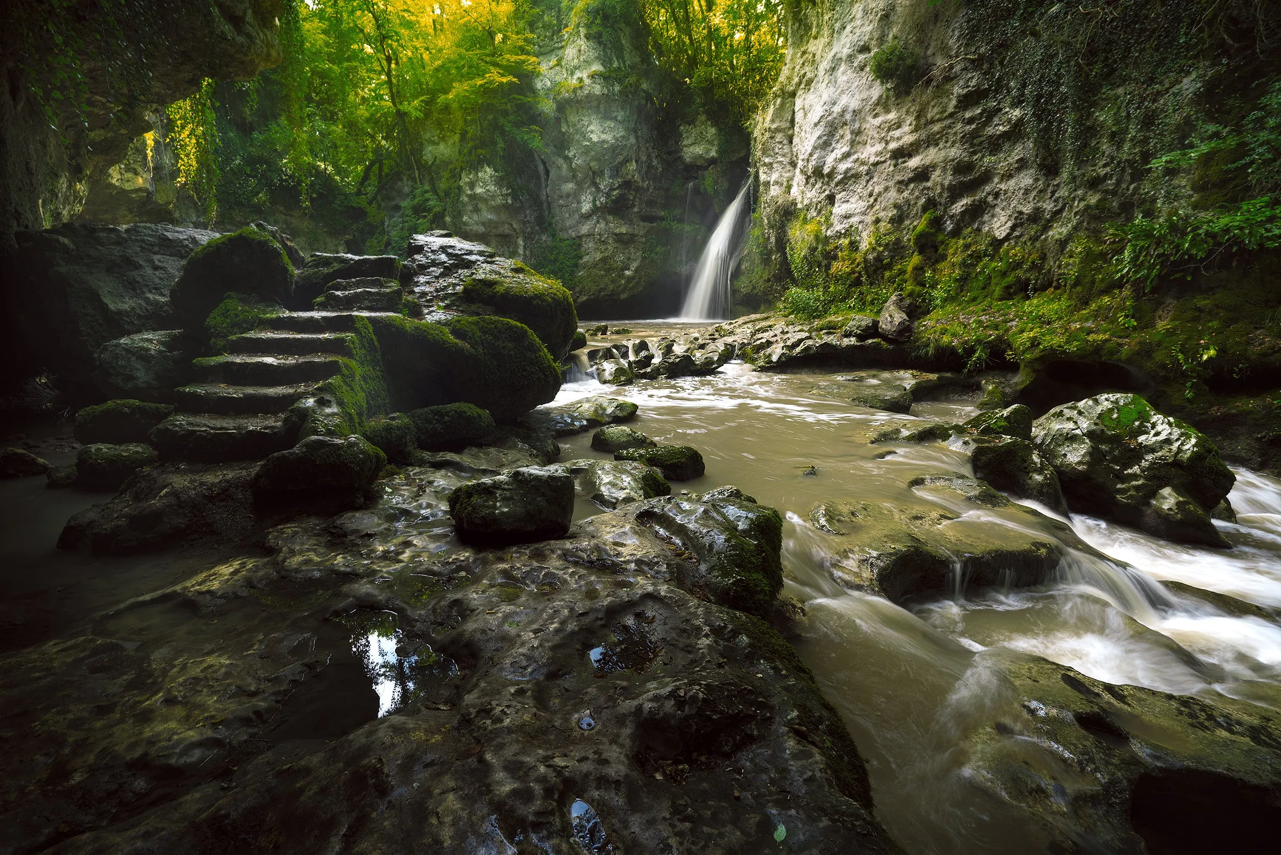 A small waterfall meeting a rocky, moss-lined stream.