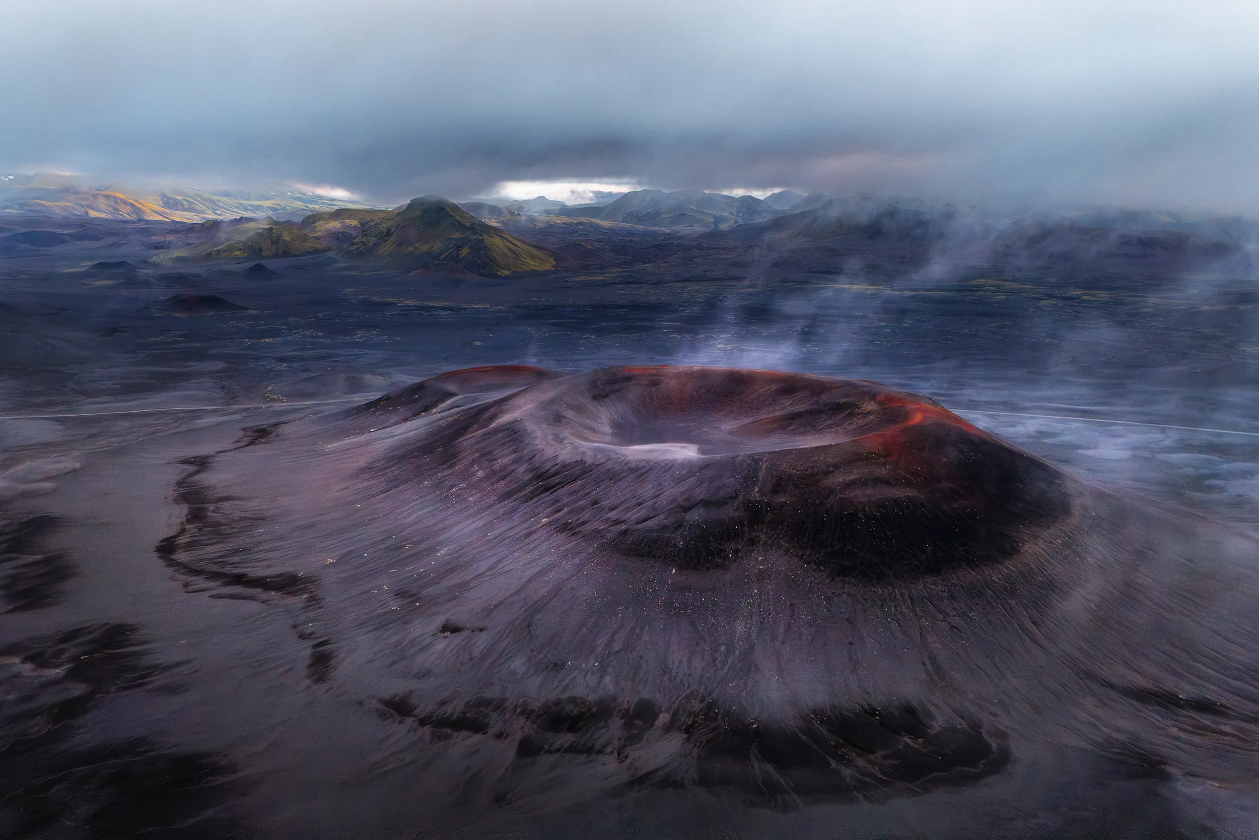 Volcano with smoke rising from its crater, surrounded by dark lava fields.