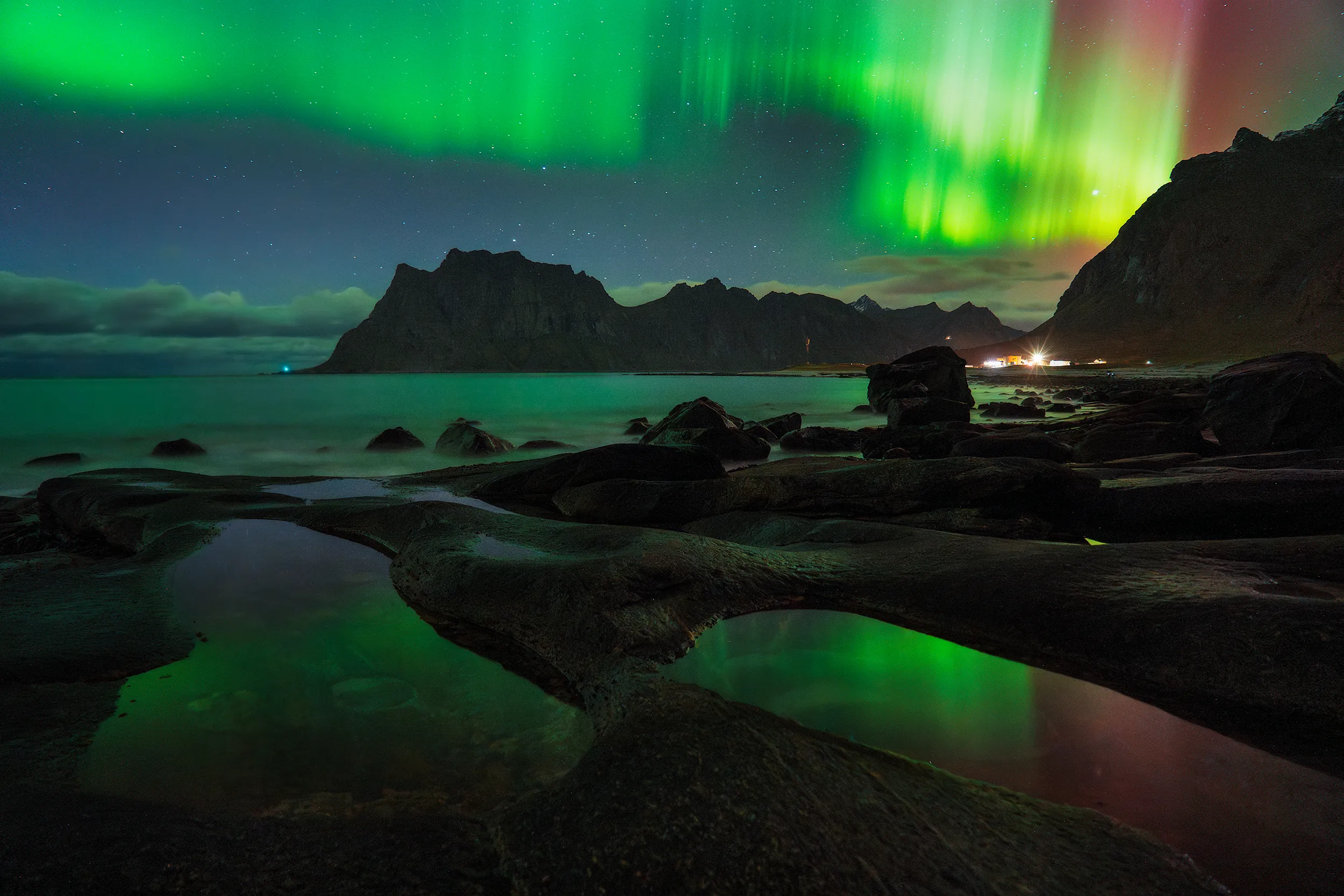 Northern lights over a rocky shoreline at night.