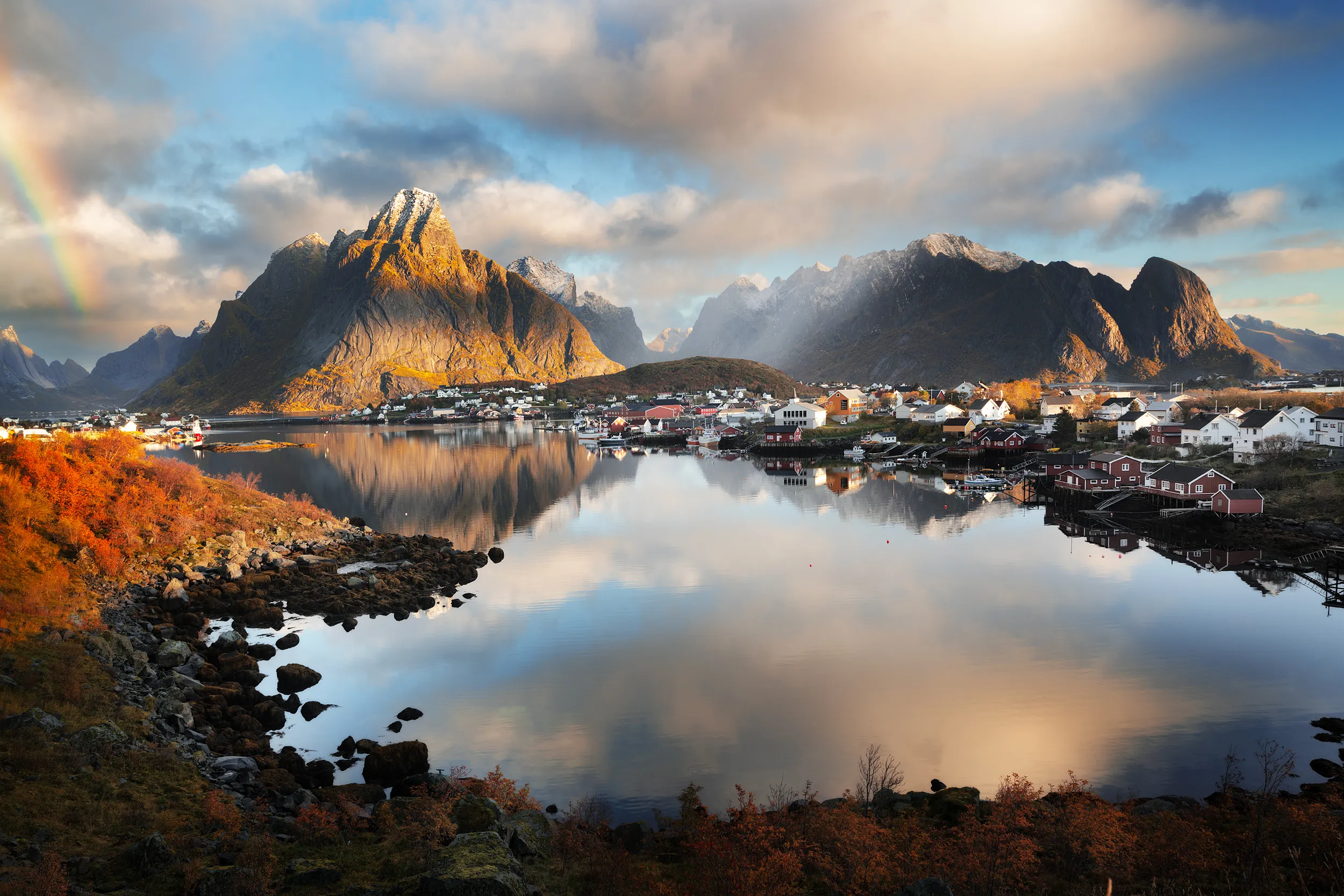 Coastal village with colorful houses, tall peaks, calm water and a rainbow.