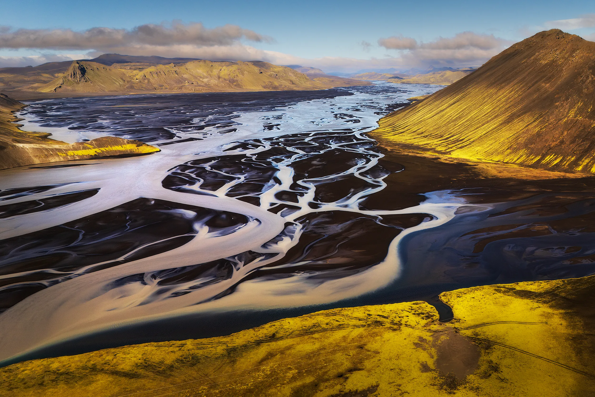 Aerial view of a black sand river with white braided channels.