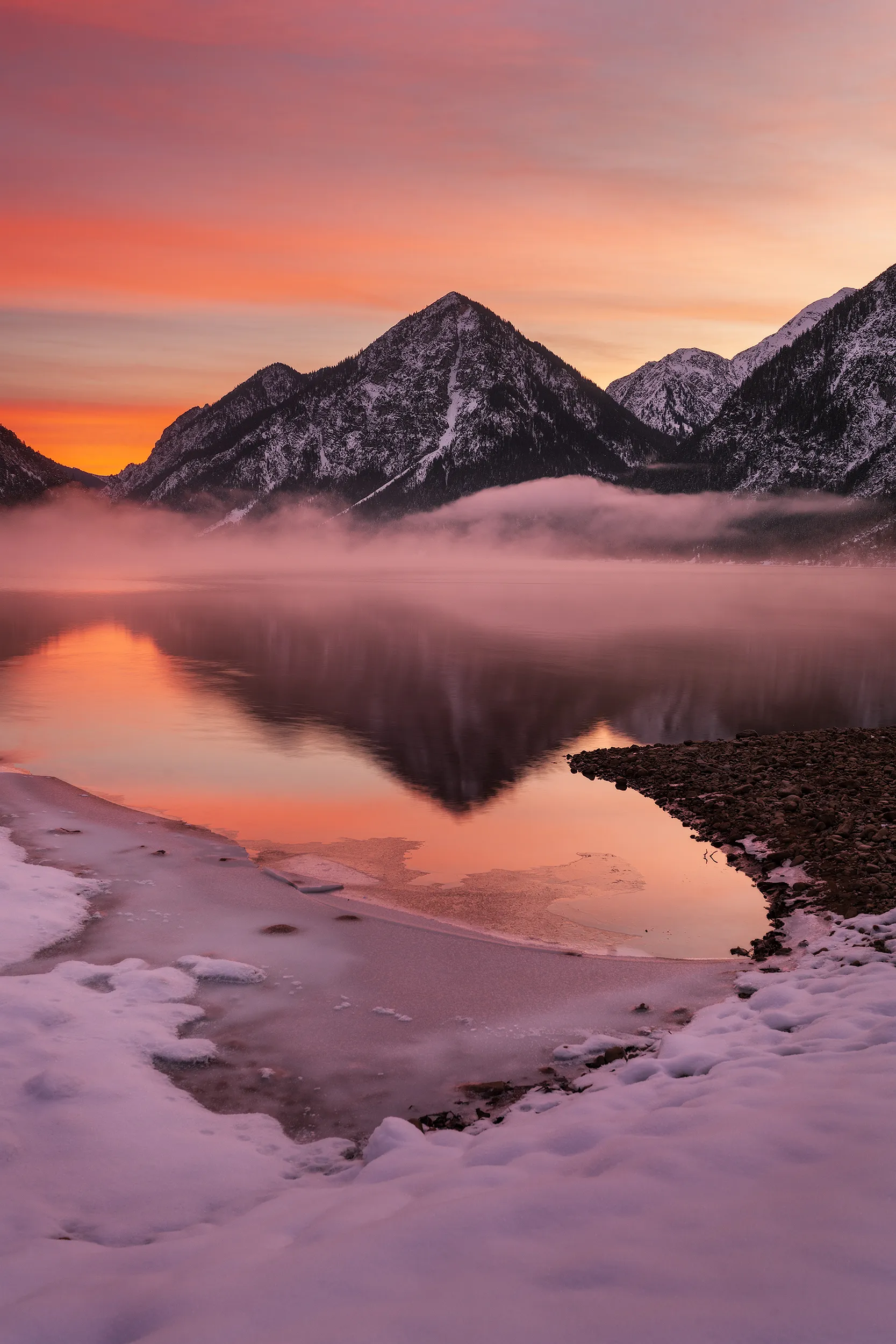 Snow-capped peaks reflected in a calm lake under a pink and orange sky.