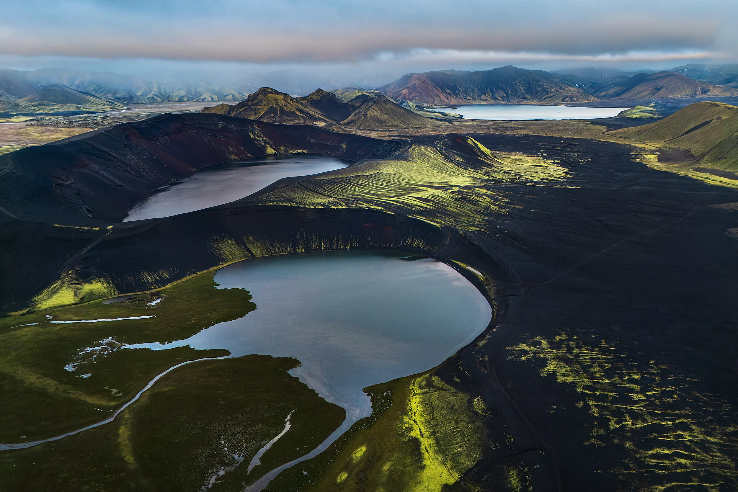 Aerial view of volcanic crater lakes in green and black terrain.